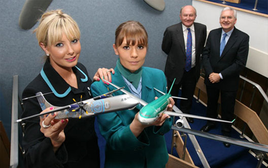 Image: Two female air stewards holding up model planes, with two older gentlemen in the background.